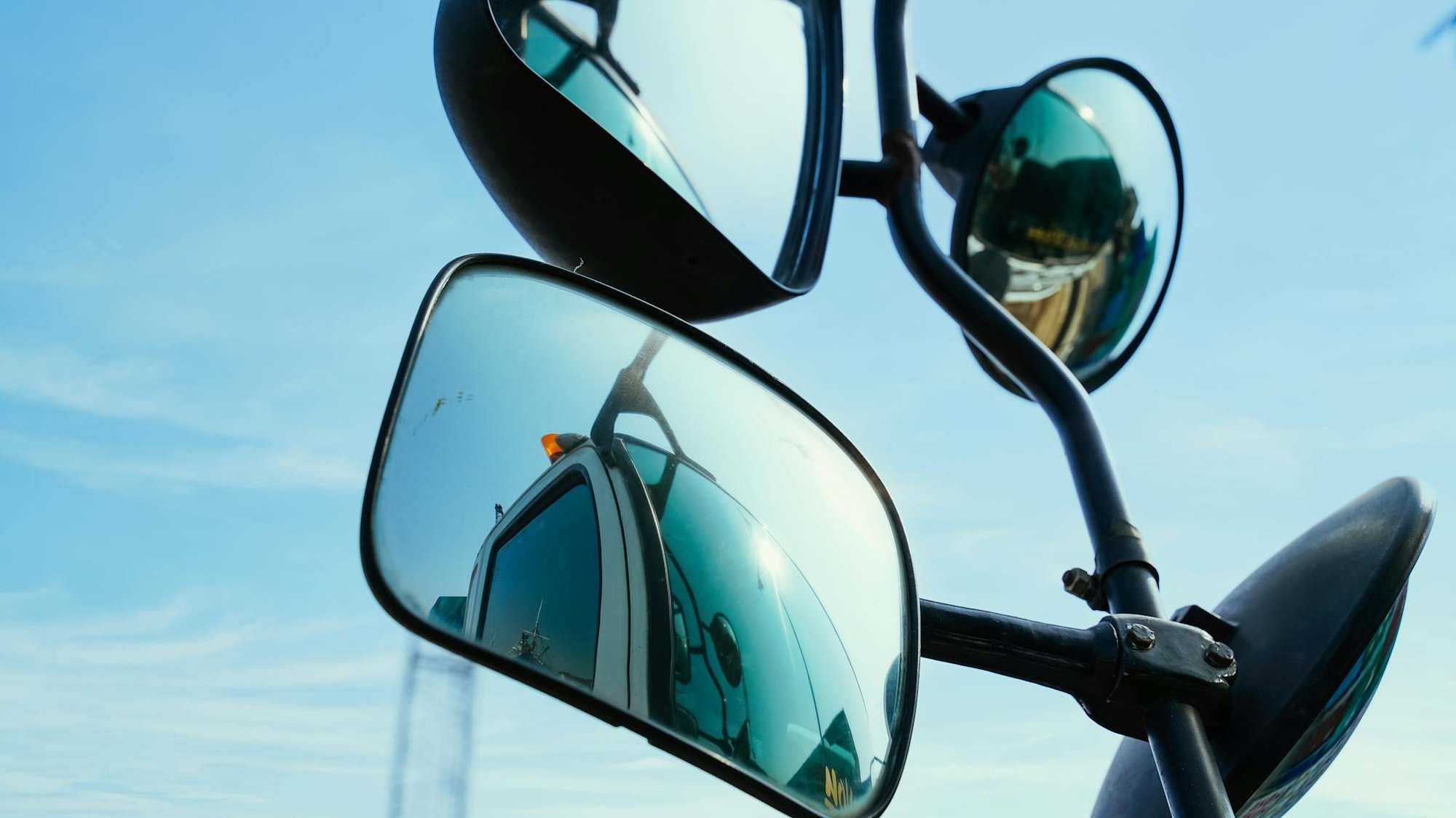Detailed view of truck mirrors reflecting clear blue sky and road.